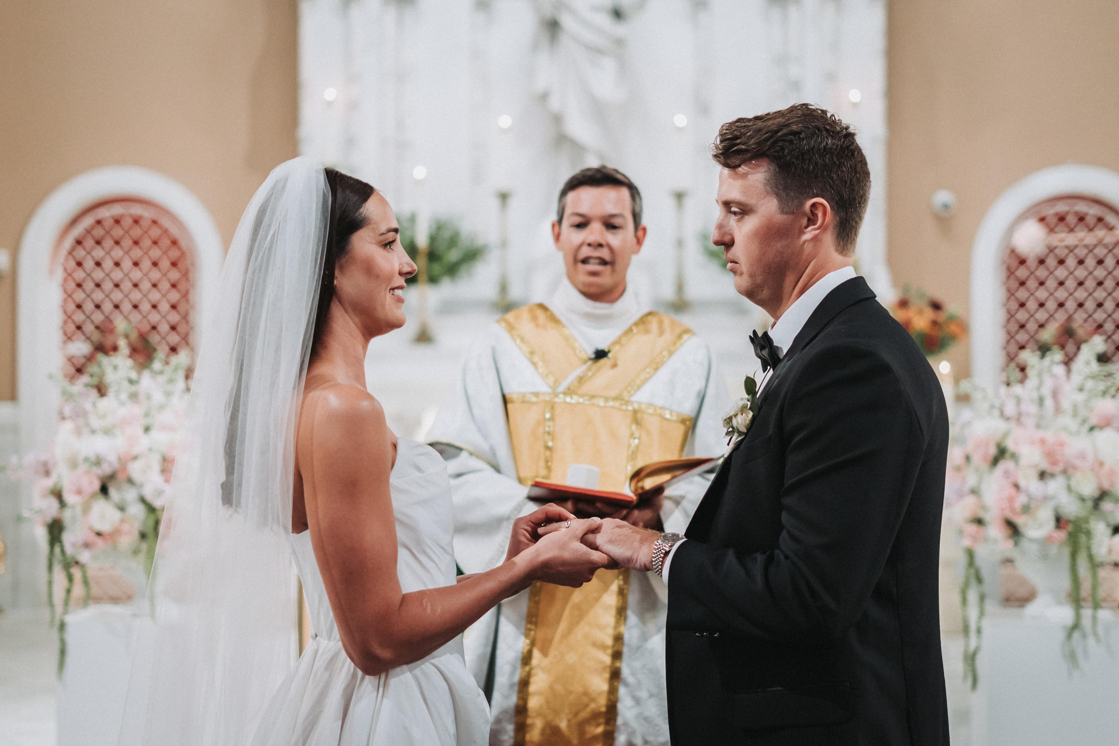 Bride and groom exchanging rings at the altar as their officiant reads from the ceremony book
