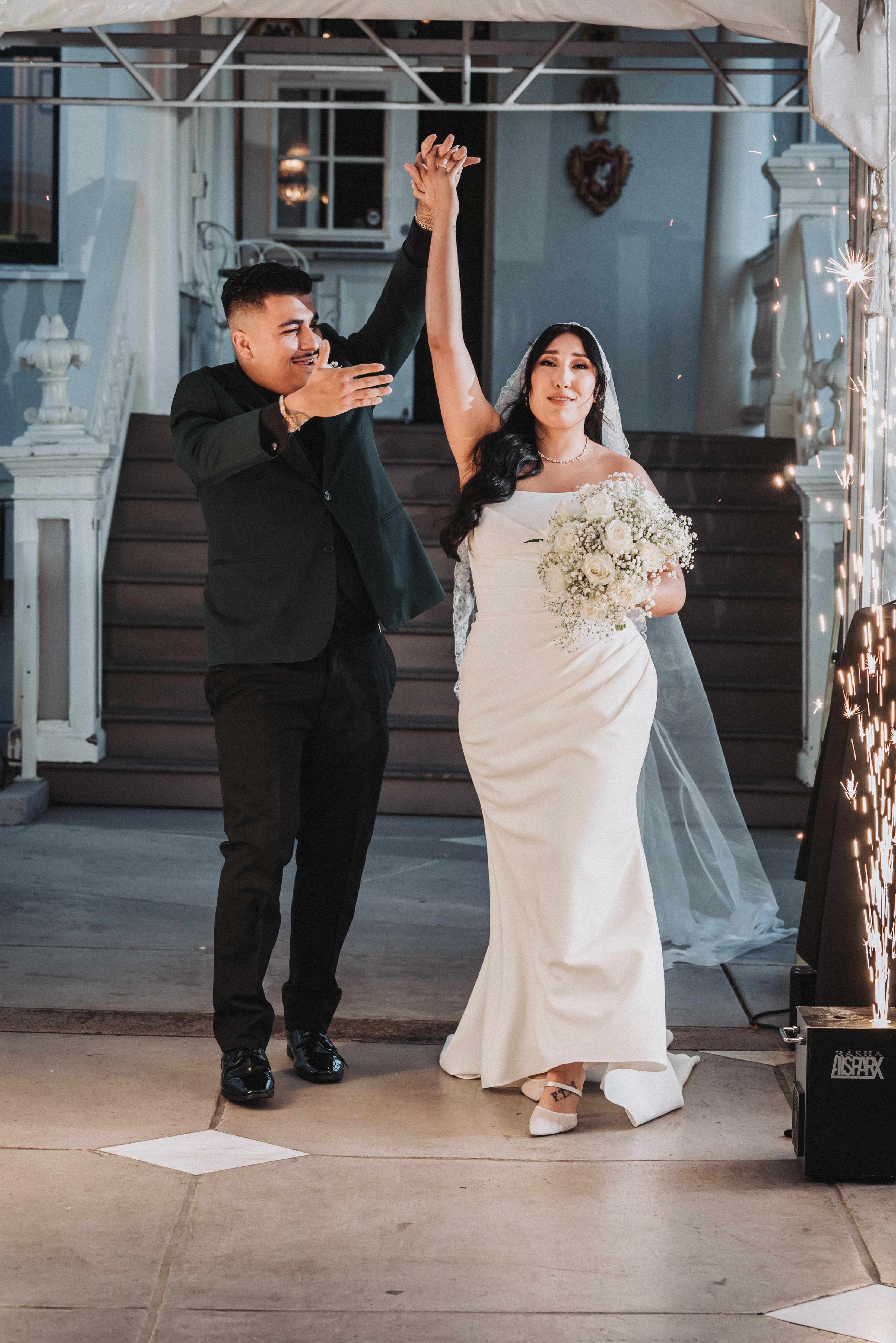Newlyweds entering their reception hand in hand as sparklers light the doorway behind them