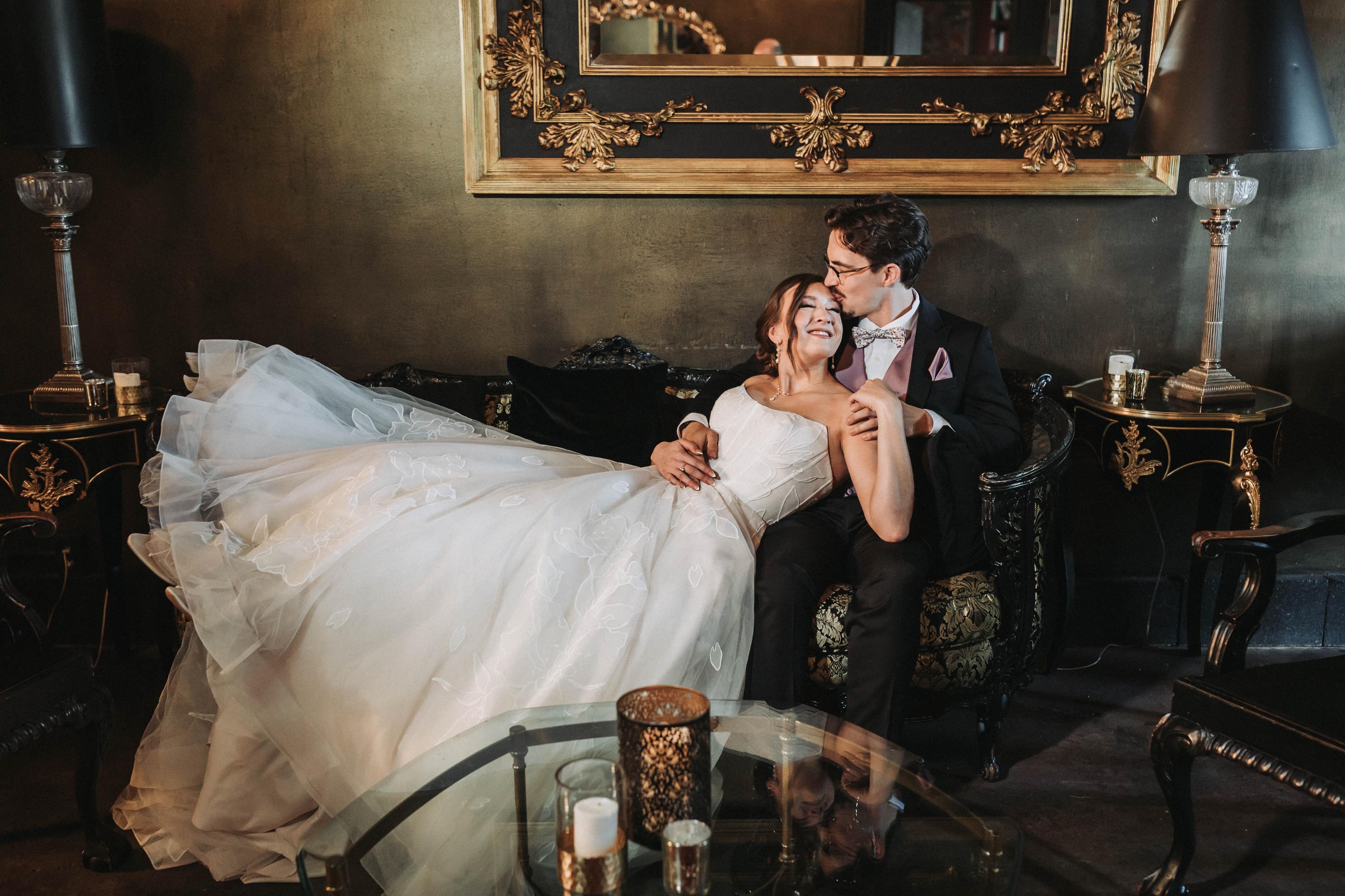 Couple resting together on an antique sofa in candlelight, the bride's train spread across the floor